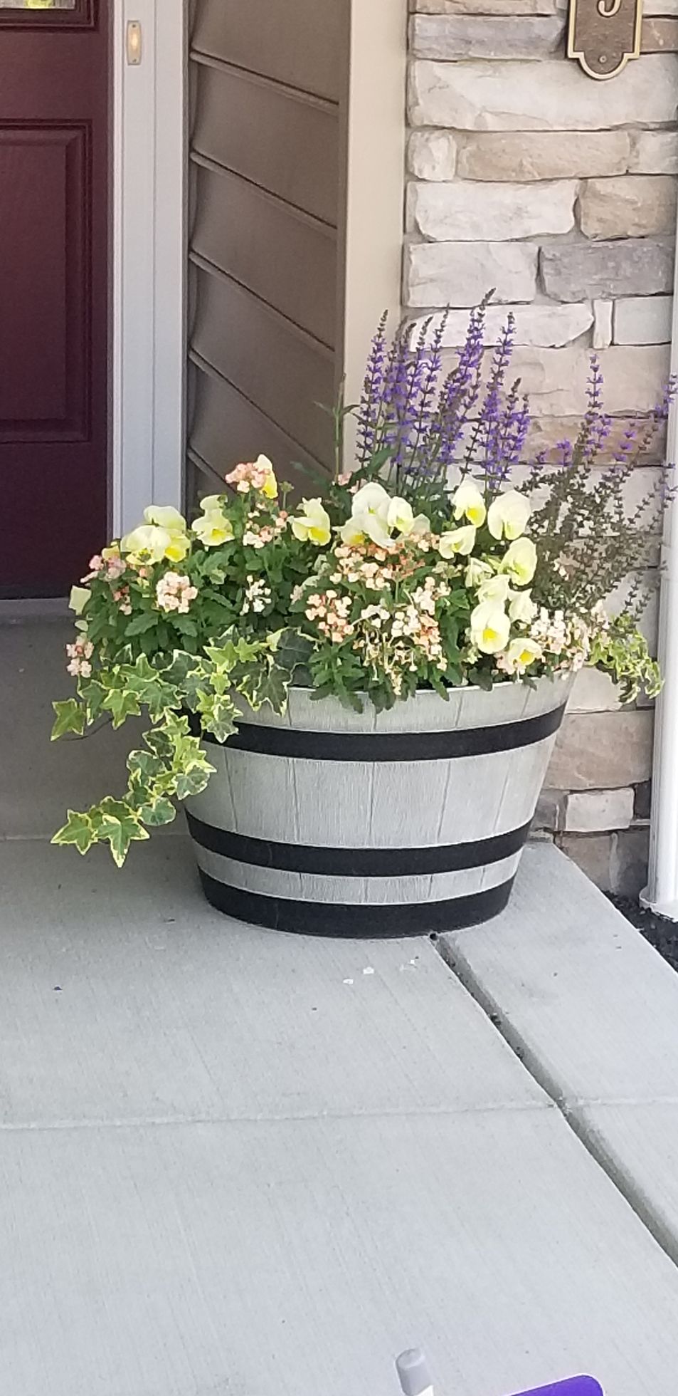 A barrel filled with flowers is on a porch next to a door.