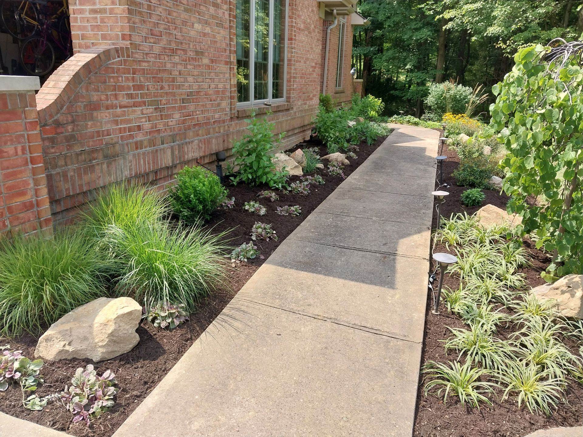 A sidewalk leading to a brick house surrounded by plants and rocks.