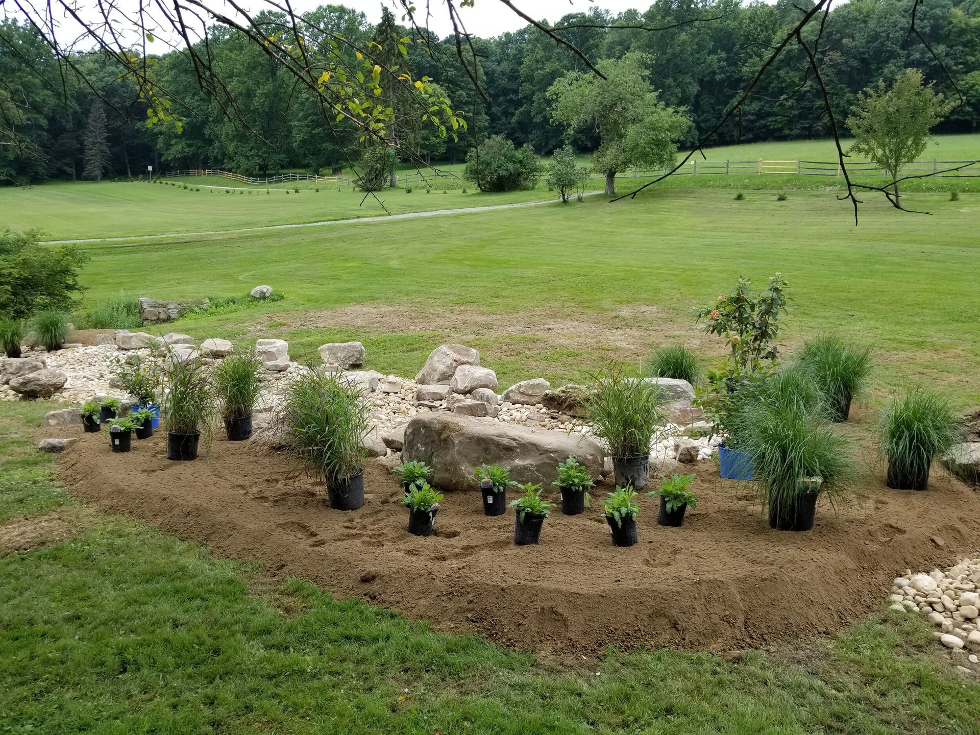 A garden with potted plants and rocks in the middle of a grassy field.