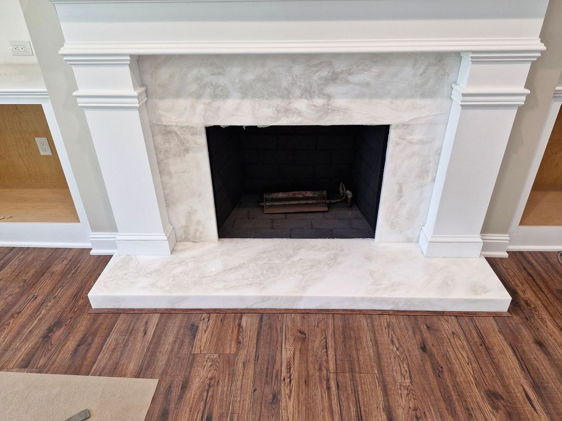 Fireplace with marble surround and wooden mantel in a room with wood flooring.