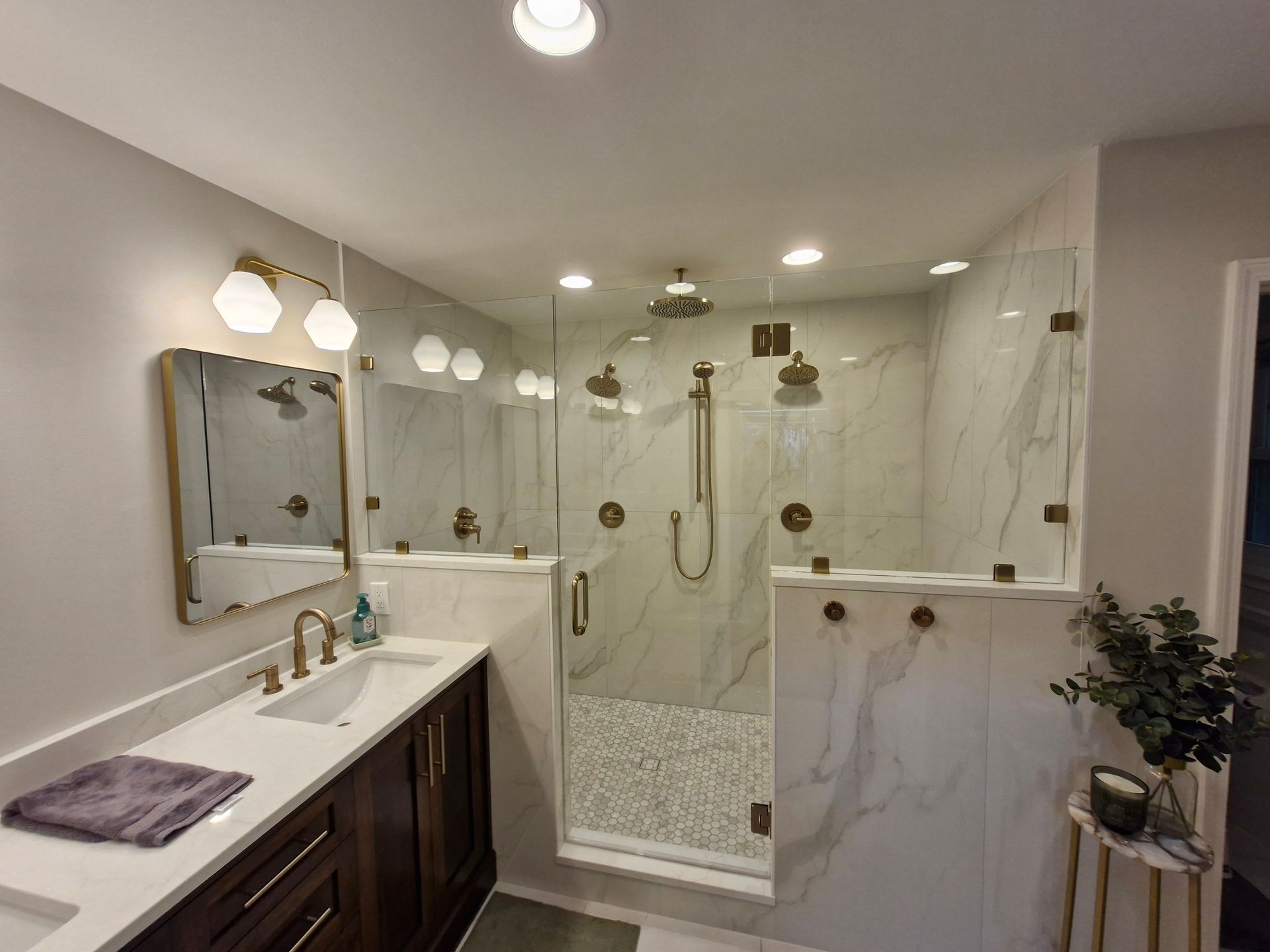 Bathroom with a walk-in shower. Marble tile walls, gold fixtures, glass doors, and a vanity.