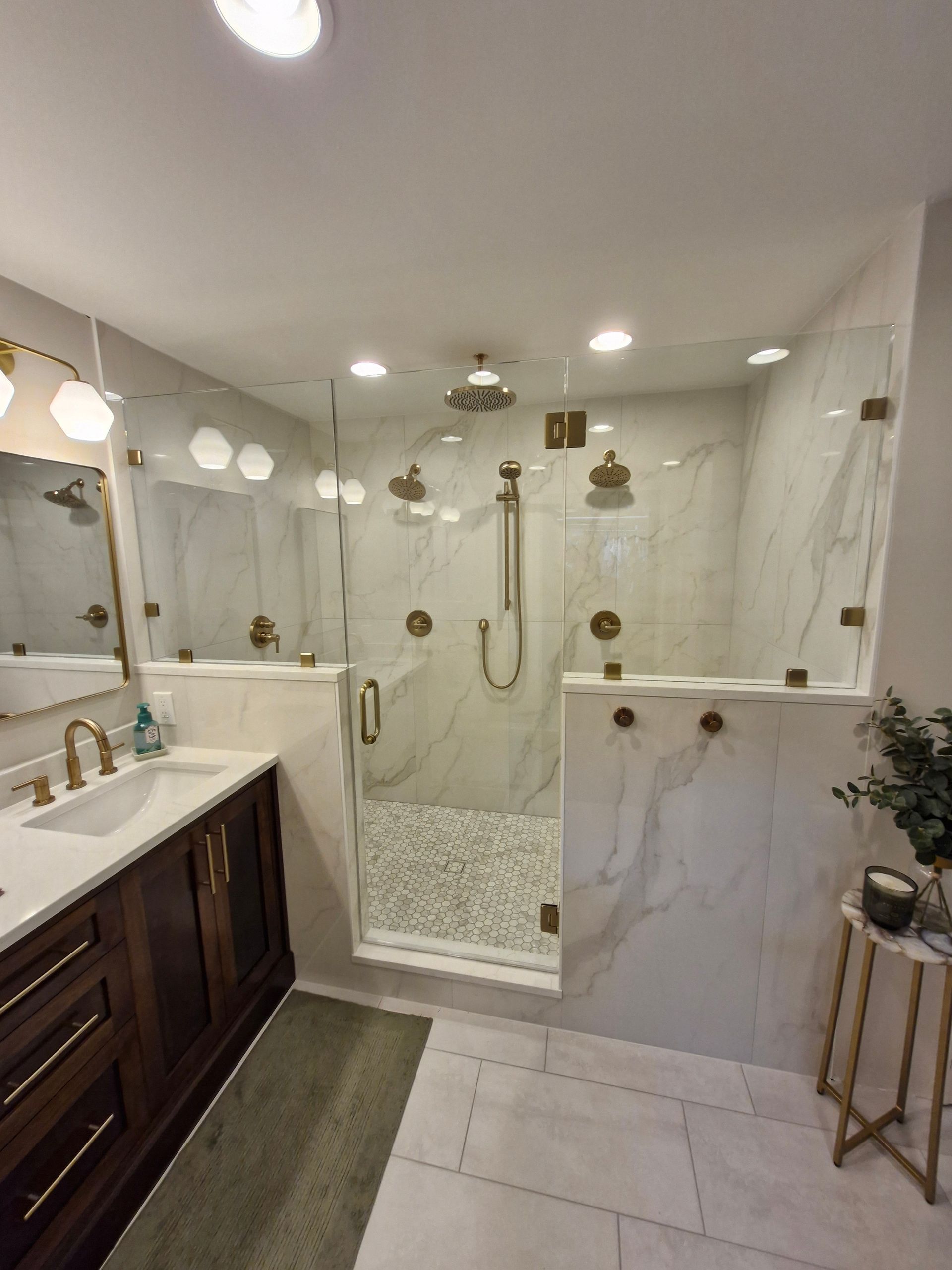 Bathroom with glass-enclosed shower, marble-look tile, dark wood vanity with gold fixtures.