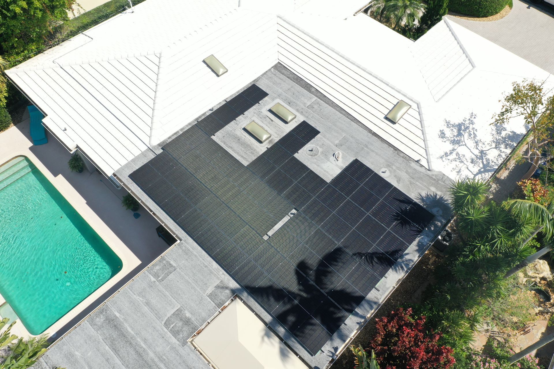 Aerial view of a house with a dark roof, white walls, and a turquoise swimming pool beside a patio.