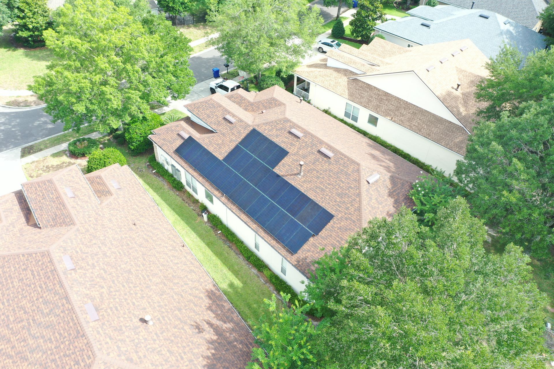 Aerial view of houses with tan roofs and solar panels, surrounded by green trees.