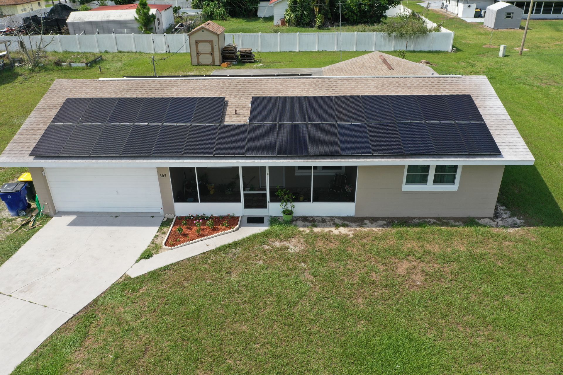 Aerial view of a single-story house with solar panels on the roof and a front lawn.