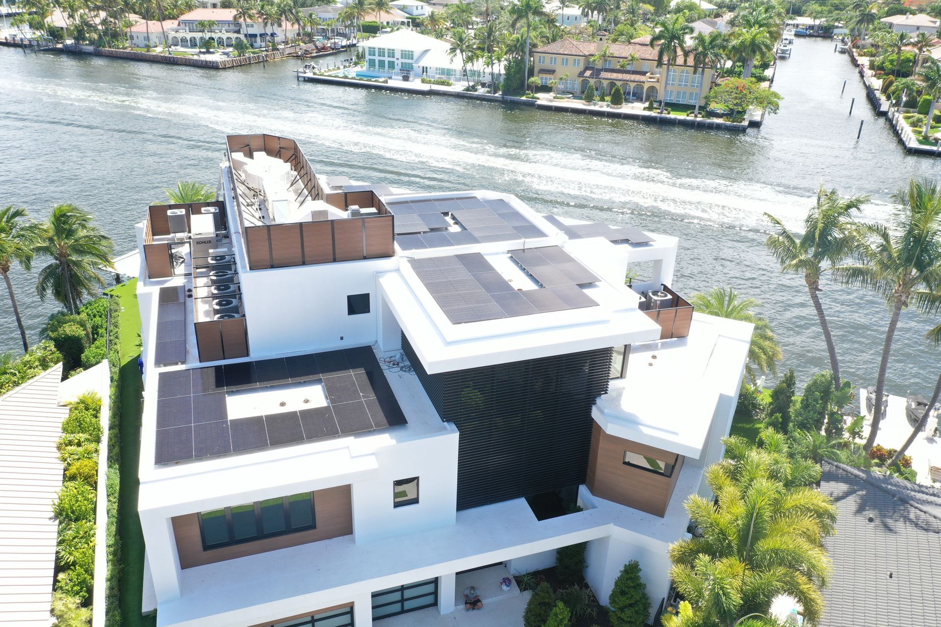 Aerial view of a modern white waterfront house with a flat roof and surrounding palm trees.