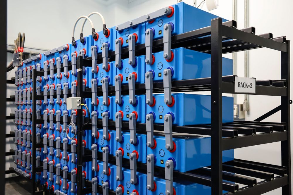 Rows of blue battery modules mounted on black racks with cables in an industrial battery storage system
