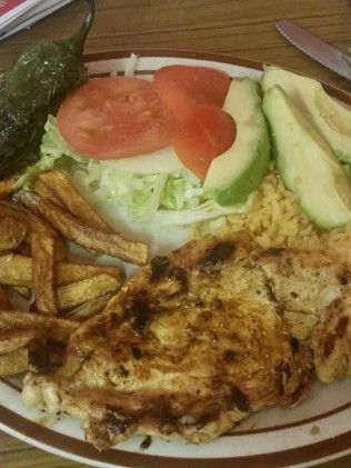 A plate of food with chicken, french fries, avocado, tomatoes, and lettuce on a table.