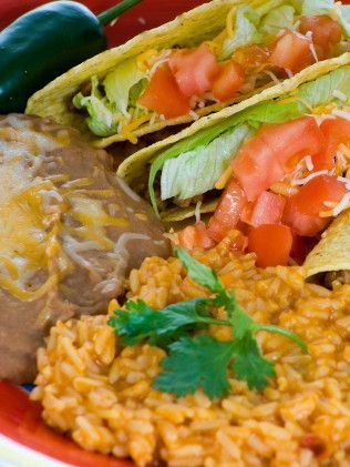 A close up of a plate of tacos, rice, and refried beans.