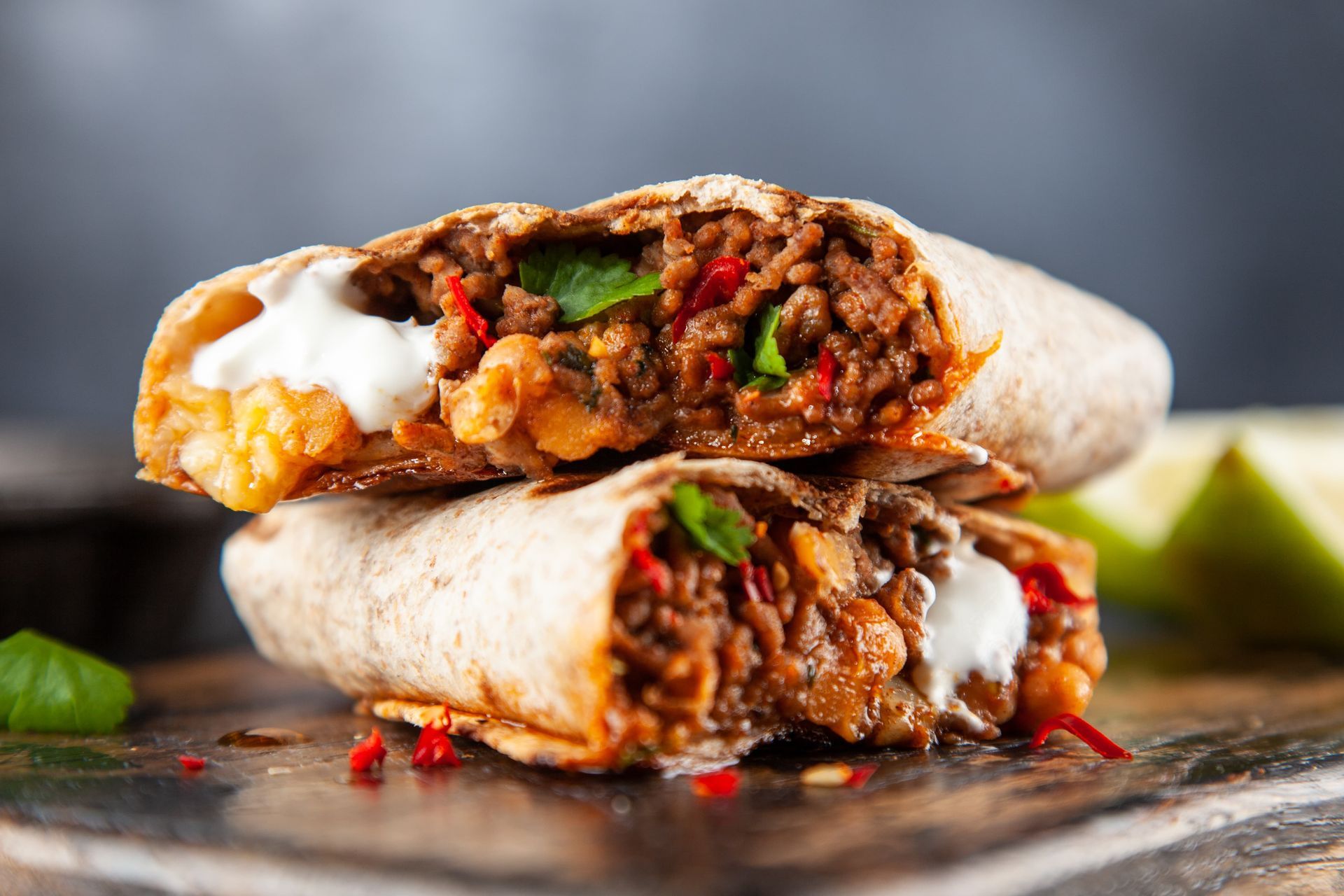 Two burritos are stacked on top of each other on a wooden cutting board.