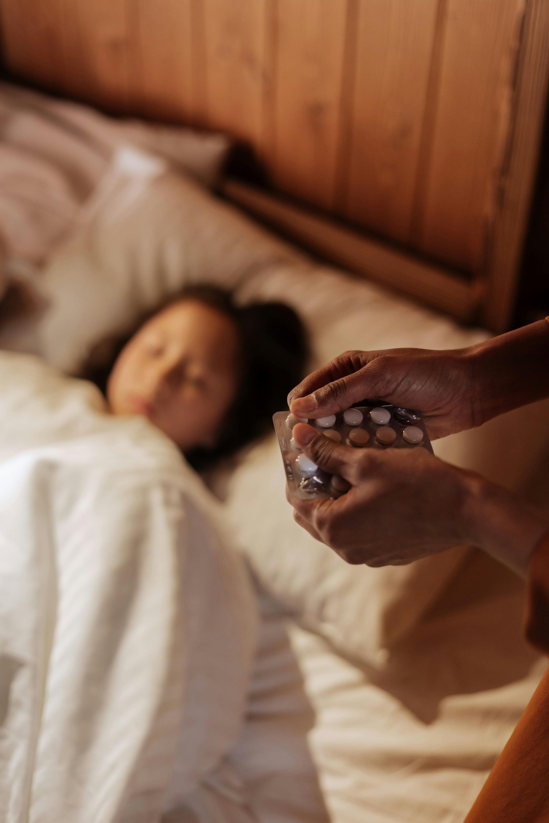 Mother's hands holding medicine with child sleeping in bed.