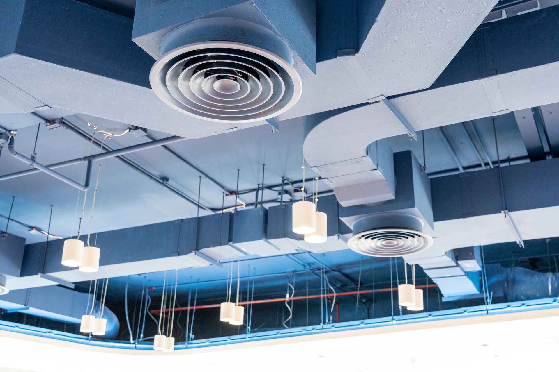 Blue ceiling with ventilation ducts, circular vents, and hanging white lights.
