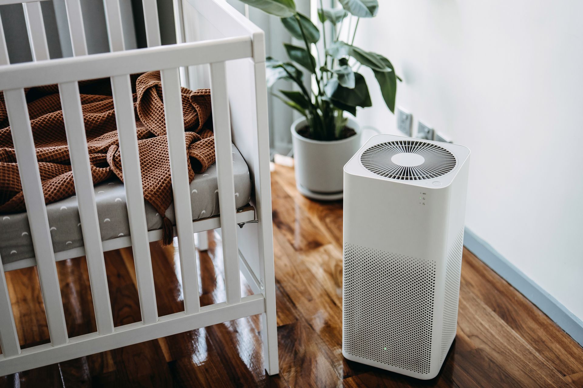White air purifier next to a crib with a blanket. Plant in the background.