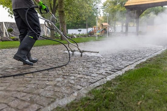 A man is using a high pressure washer to clean a brick walkway.