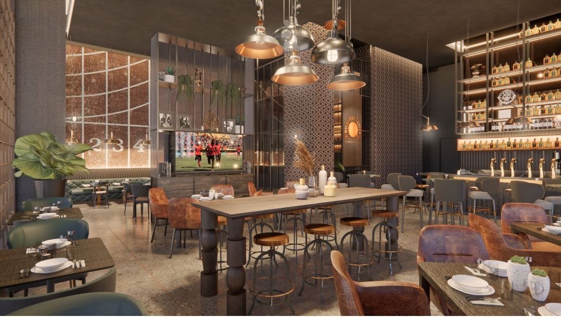 Restaurant interior with long table, bar, and seating. Warm lighting, brick walls, and a TV.