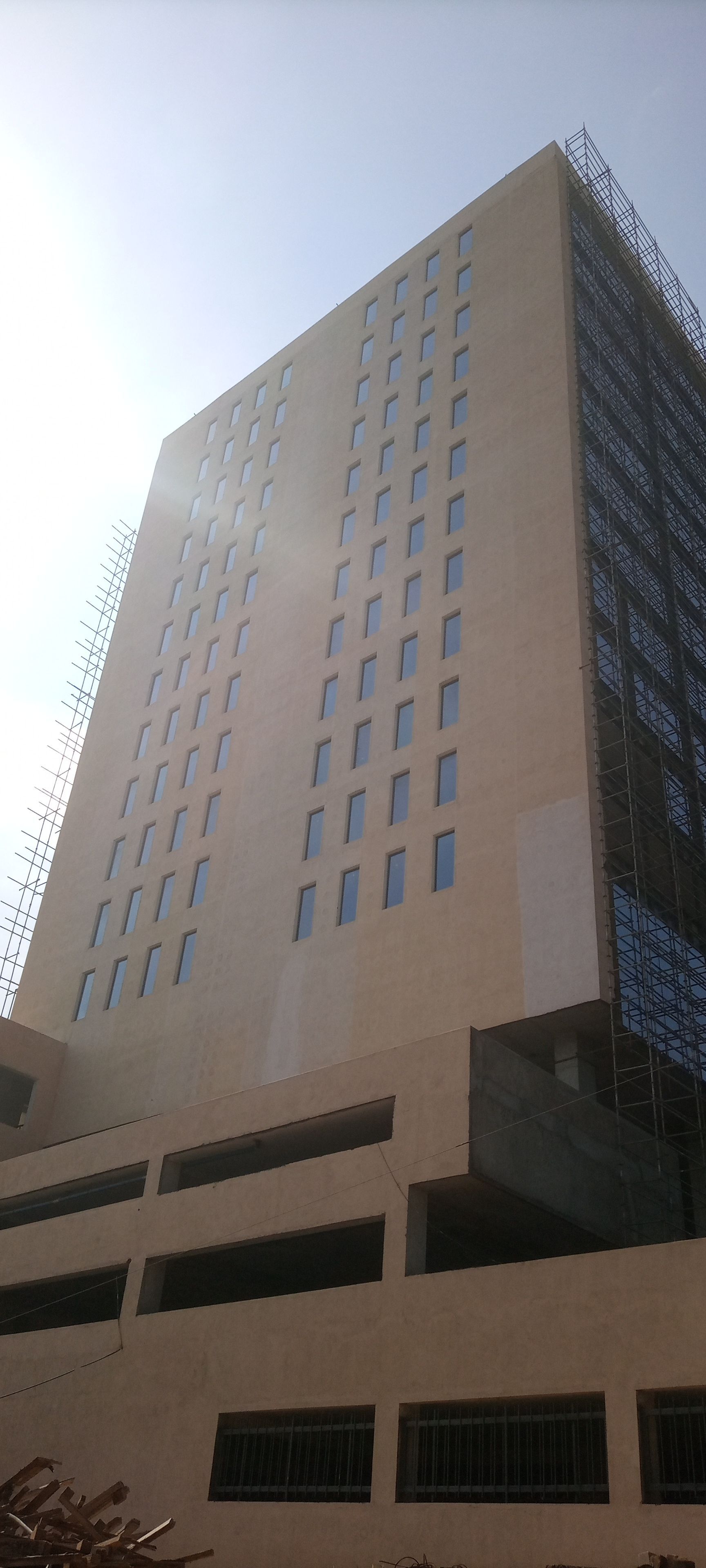 A tall, beige high-rise building with many rectangular windows. The sky is a clear blue.