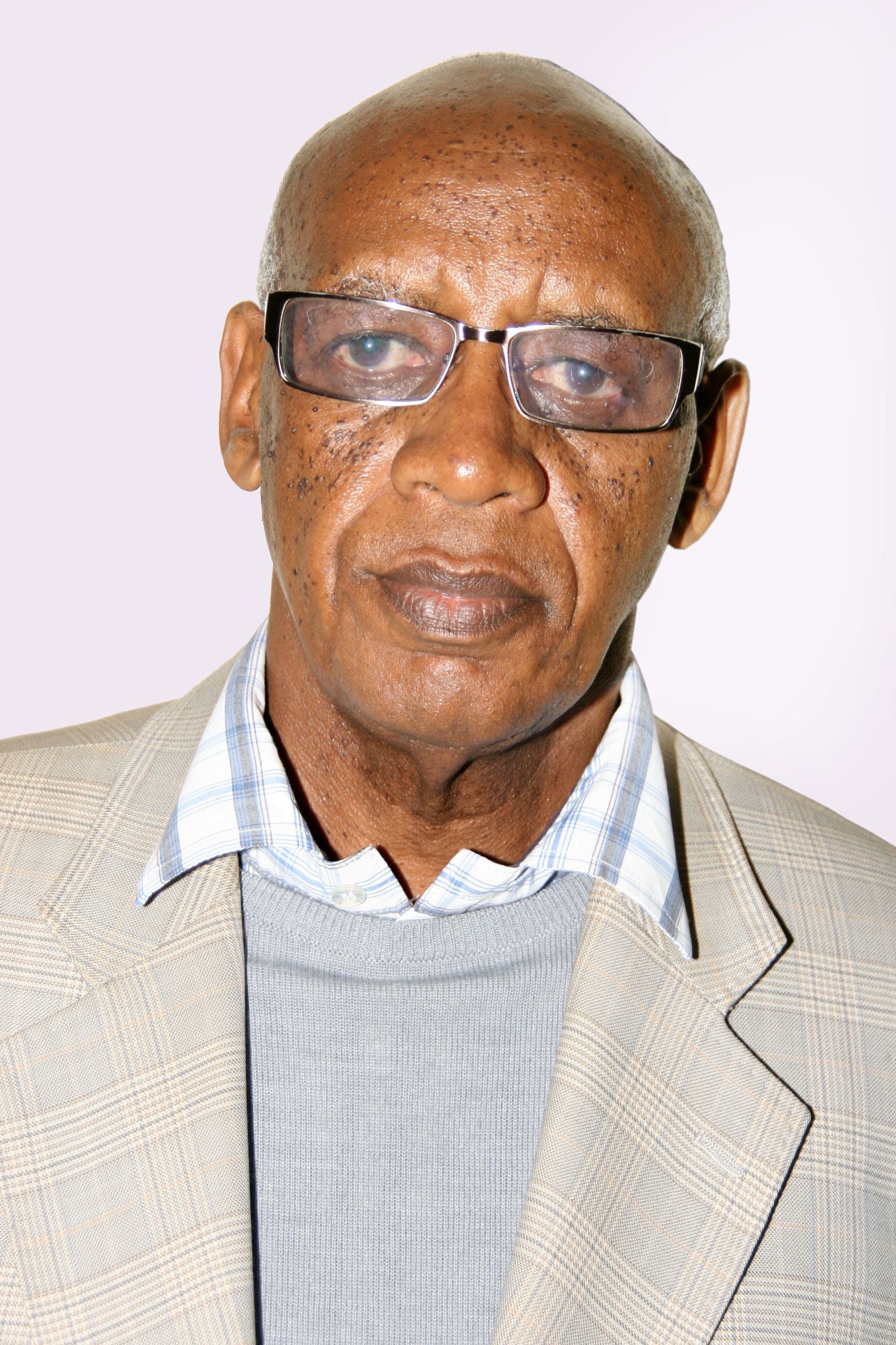 Older Black man with glasses, wearing a light tan blazer over a blue and white collared shirt.