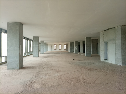 Empty concrete office space with support columns and windows along the side.