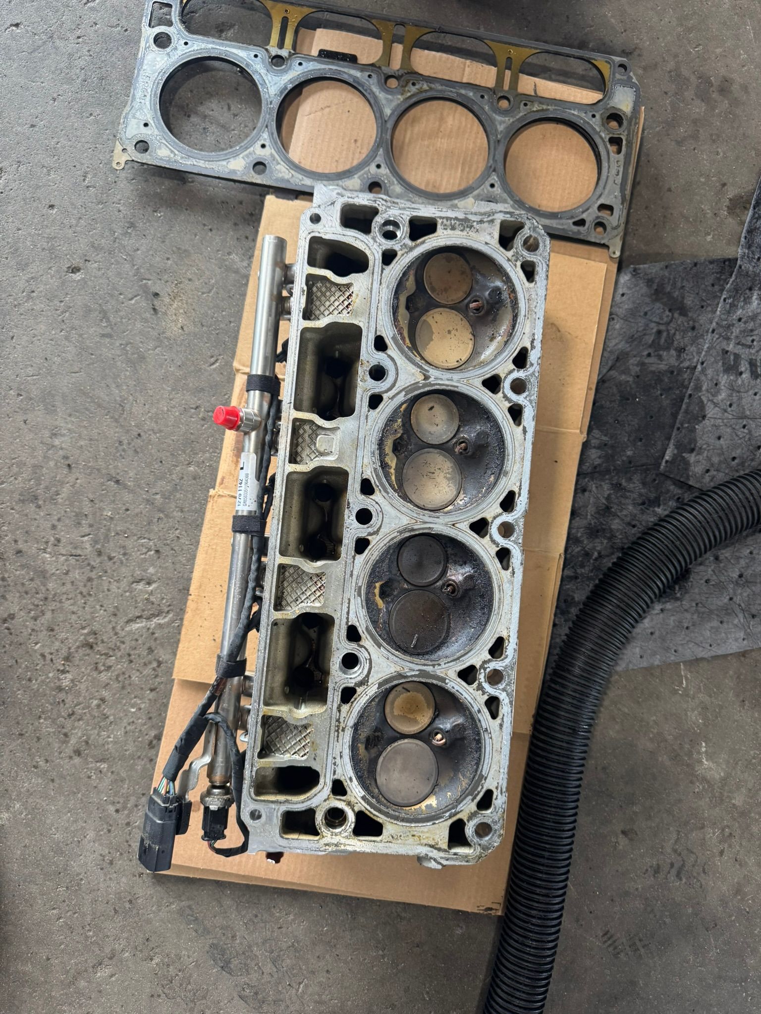 Engine cylinder head with exposed valves, on cardboard in a garage.