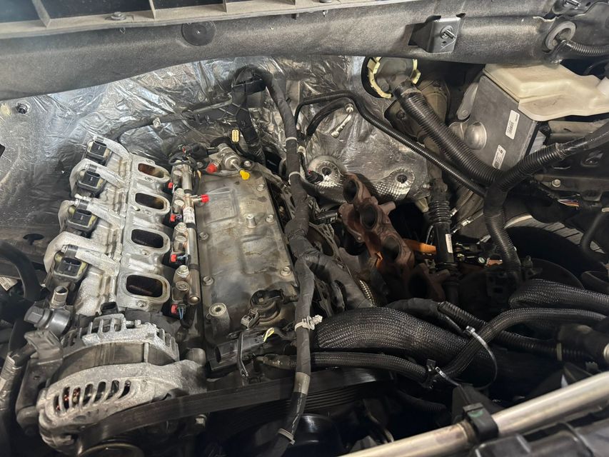 Engine bay with removed parts, showing engine block, manifolds, and wiring harnesses.