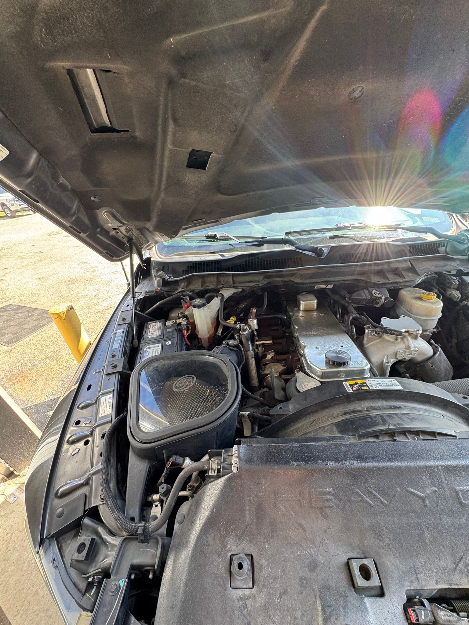 Open car hood revealing engine compartment. Black, with various components visible.