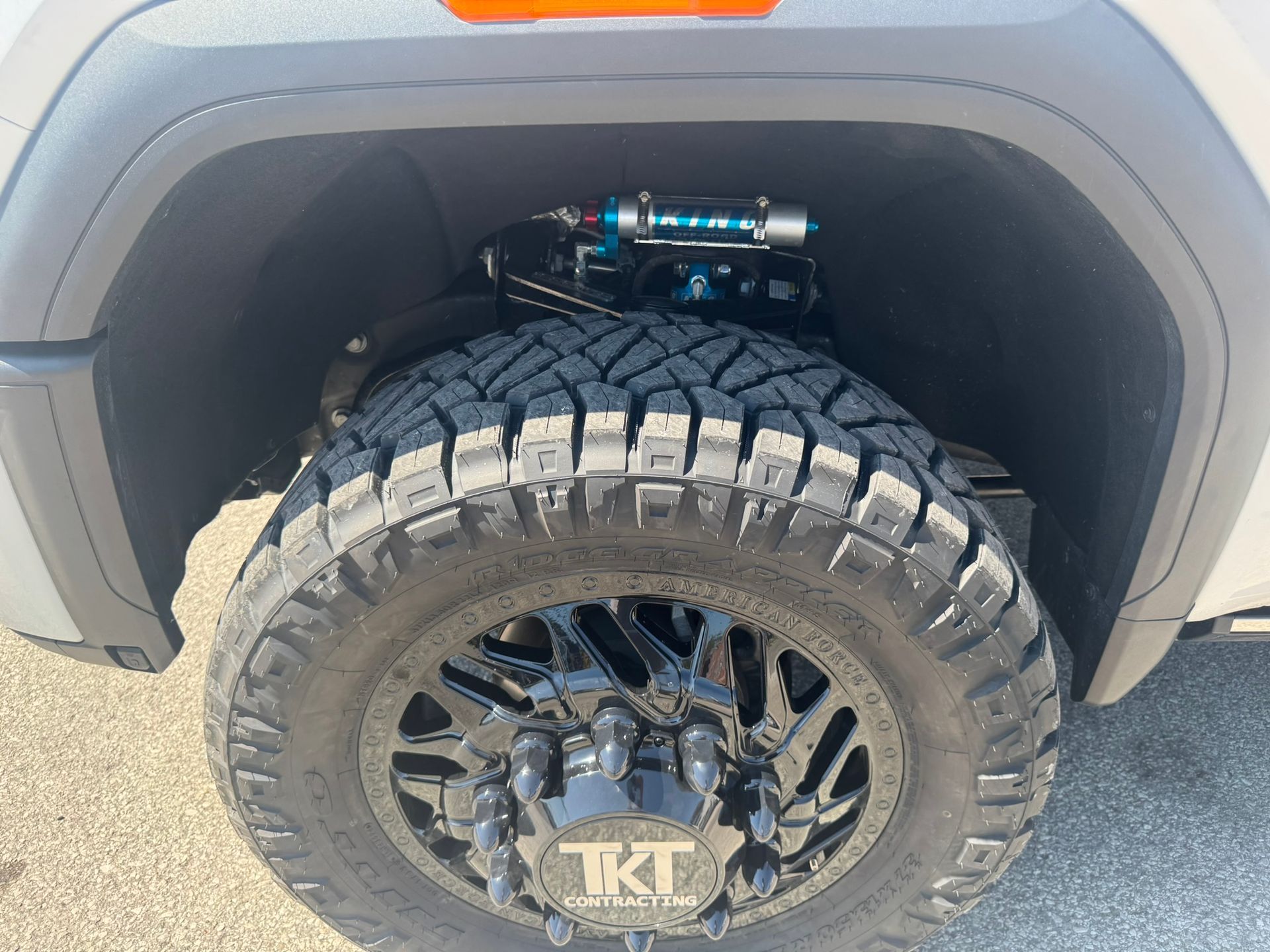 Close-up of a lifted truck tire and suspension. Black tire with black rim and blue shock.