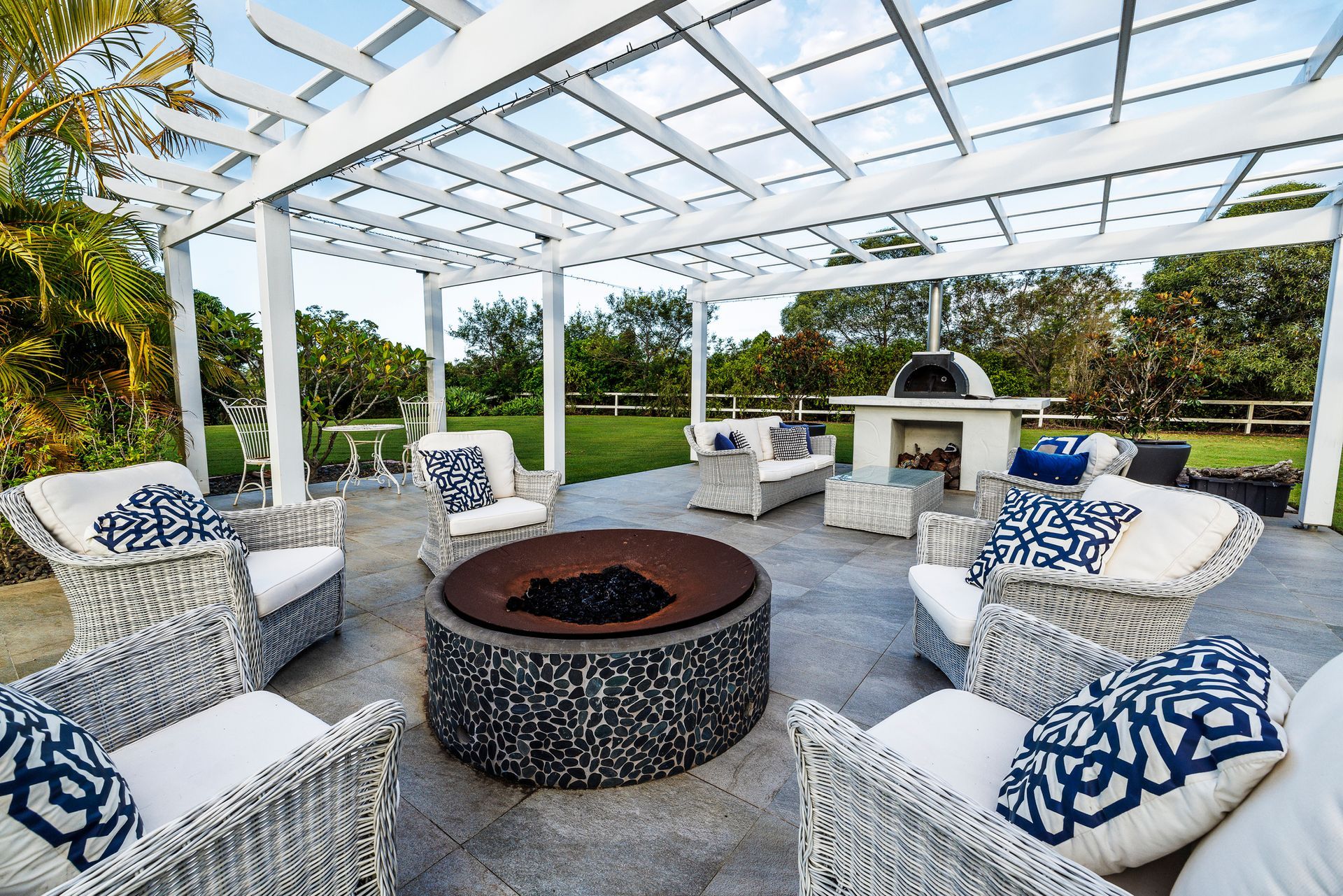 Outdoor seating area with white wicker furniture, fire pit, and pergola.