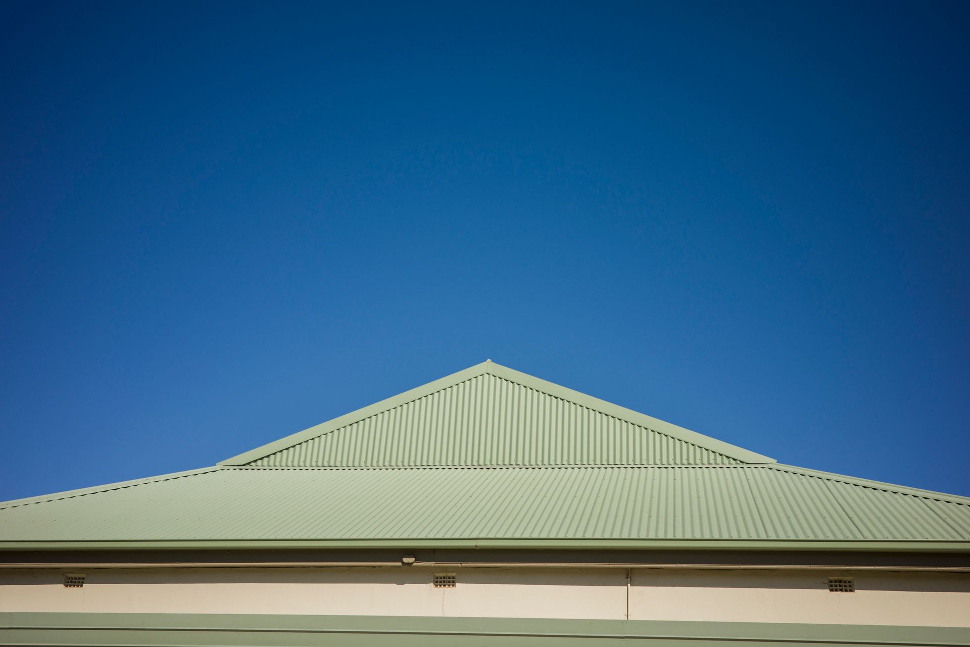 Red brick chimney on a red corrugated metal roof against a blue sky, coastal setting.