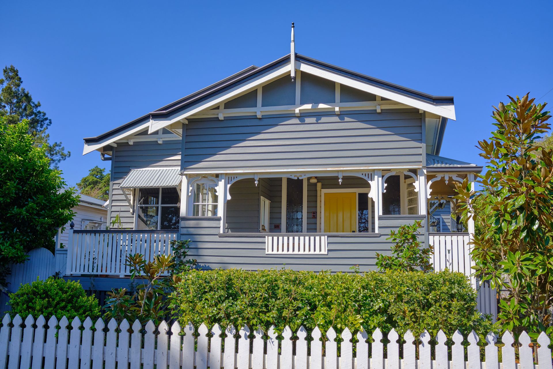 Gray house with white trim and a yellow door behind a white picket fence.