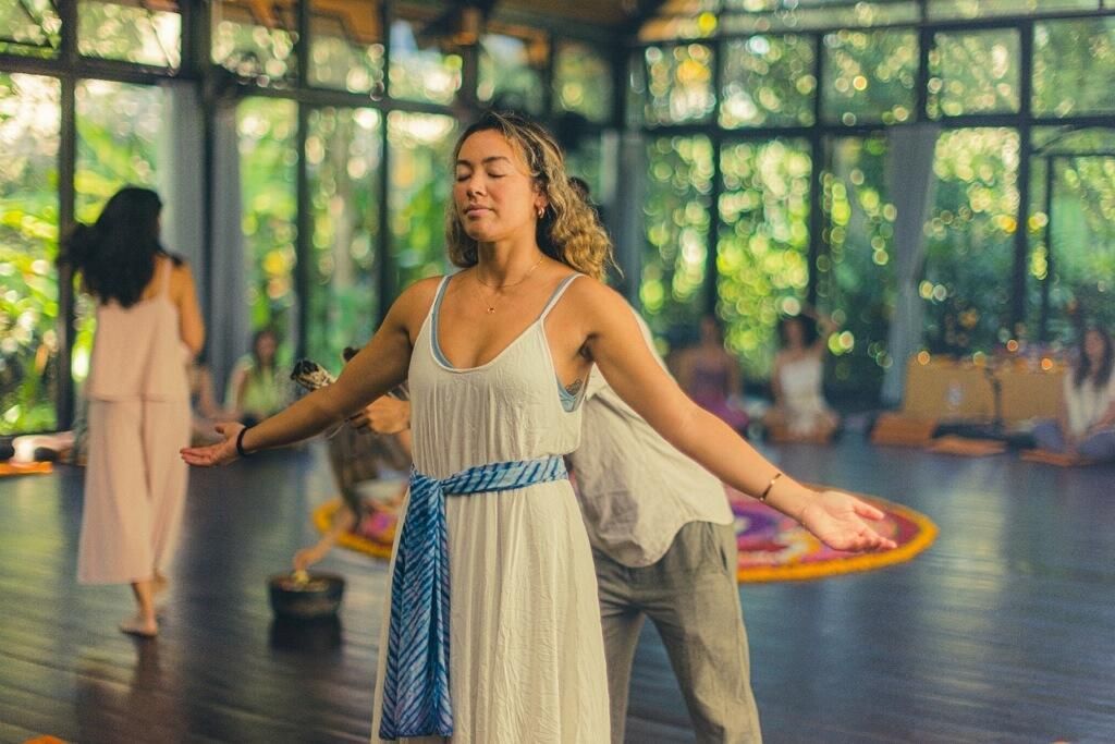 A woman in a white dress is standing in a room with her arms outstretched.