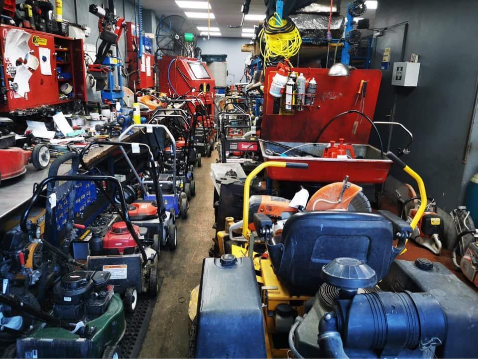 A lot of lawn mowers are in a garage.