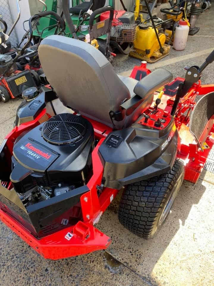 A red and black lawn mower is parked on the side of the road.
