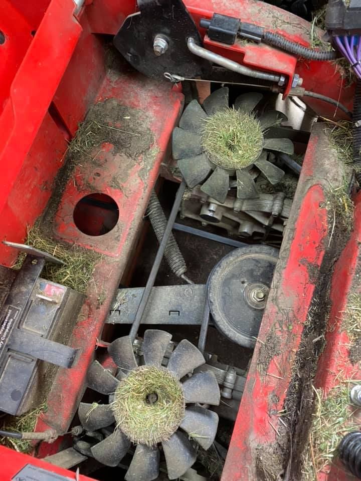The engine of a lawn mower is covered in grass and dirt.
