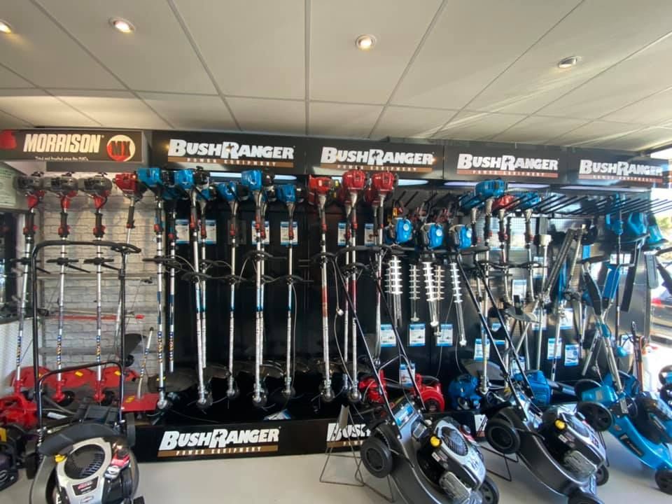 A row of bush ranger lawn mowers are lined up in a store.