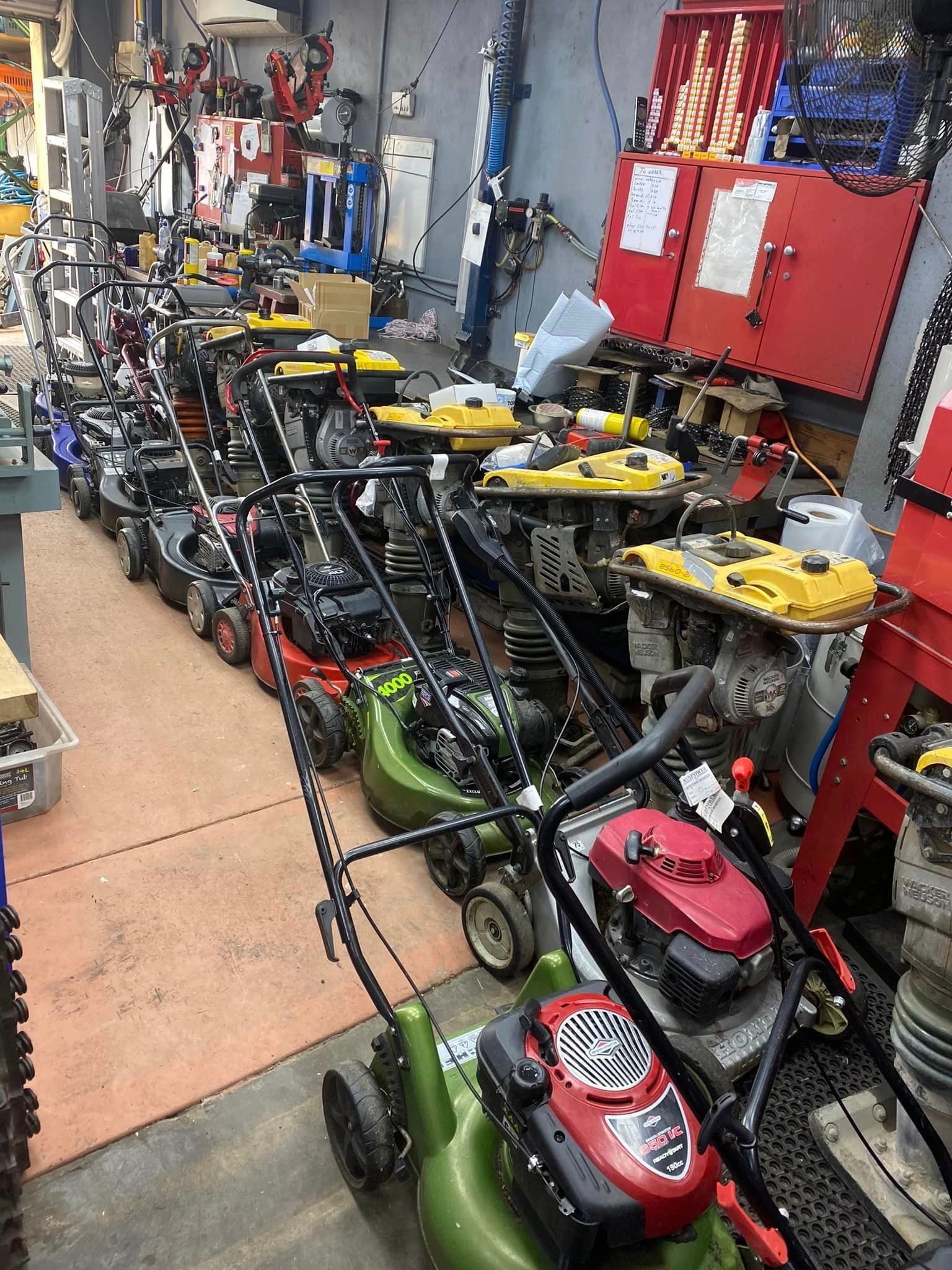 A row of lawn mowers are lined up in a garage.