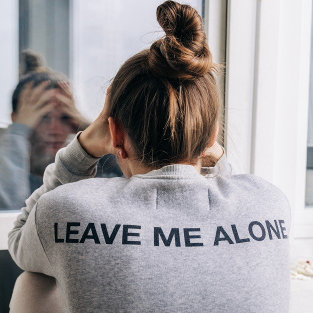 Girl sitting down depressed with leave me alone on her shirt