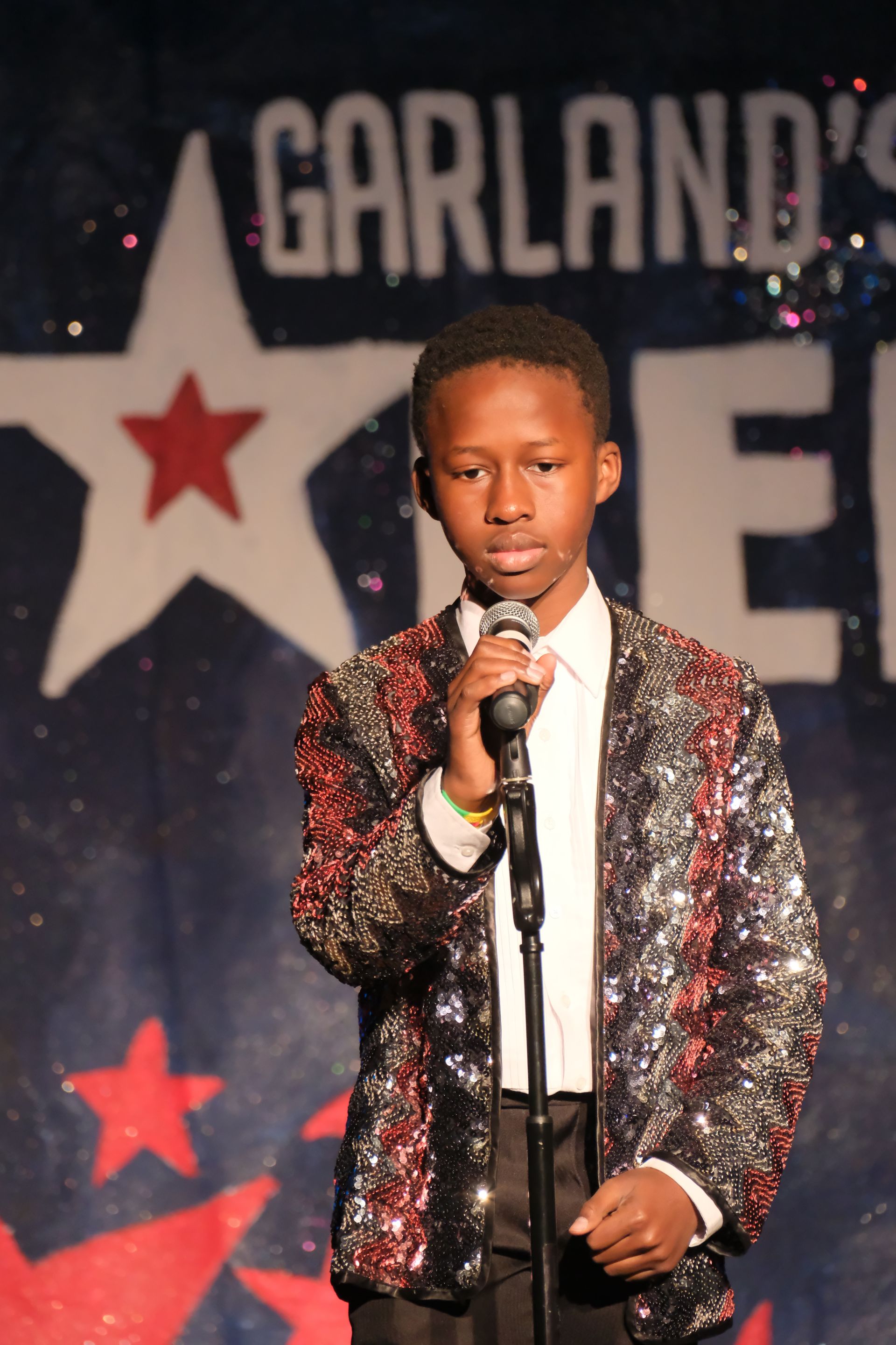 Young person in sequined jacket singing into a microphone on stage, 
