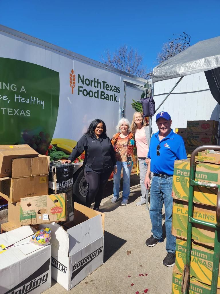 People near a North Texas Food Bank truck, surrounded by boxes of food, on a sunny day.