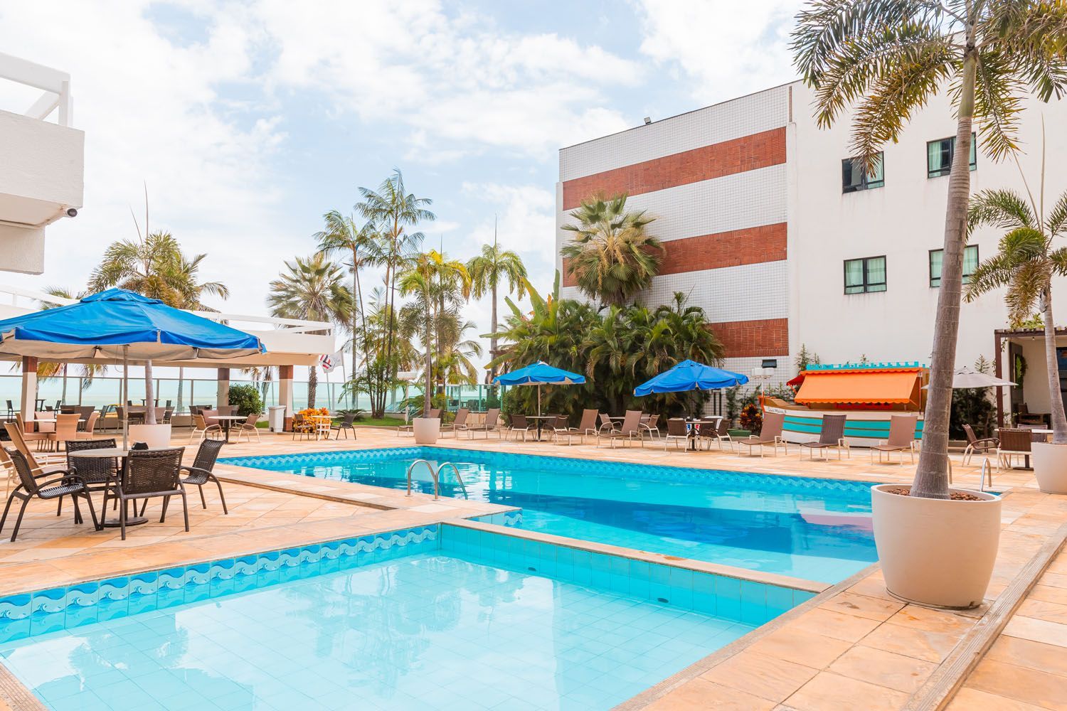 Uma grande piscina com mesas e cadeiras em frente a um prédio.