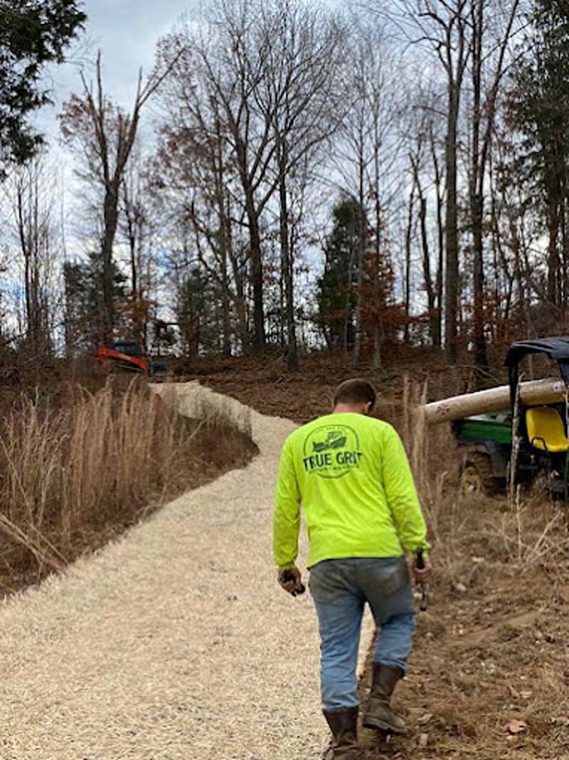 A man in a neon yellow shirt is walking down a dirt road.