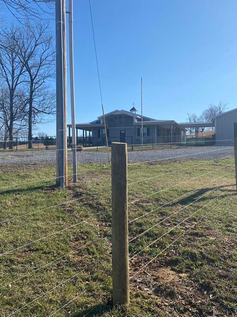 A wooden post in the middle of a grassy field with a house in the background.