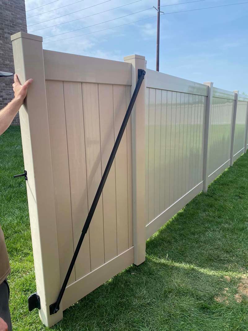 A person is standing next to a white fence in the grass.