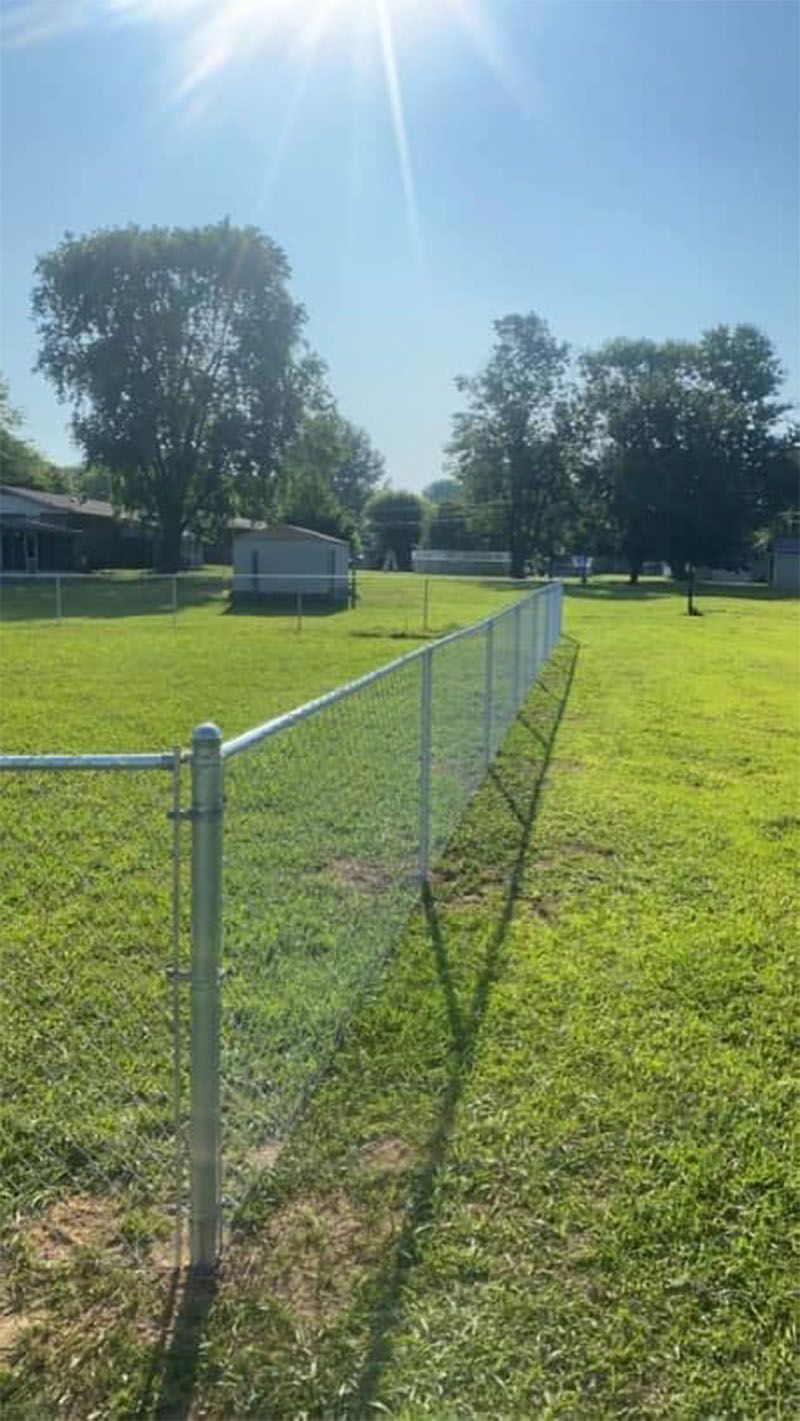 A chain link fence surrounds a lush green field.