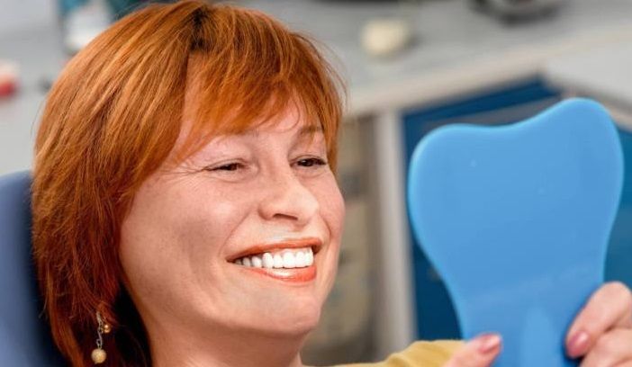 woman happy with detures looking at herself with mirror, dentist 33578