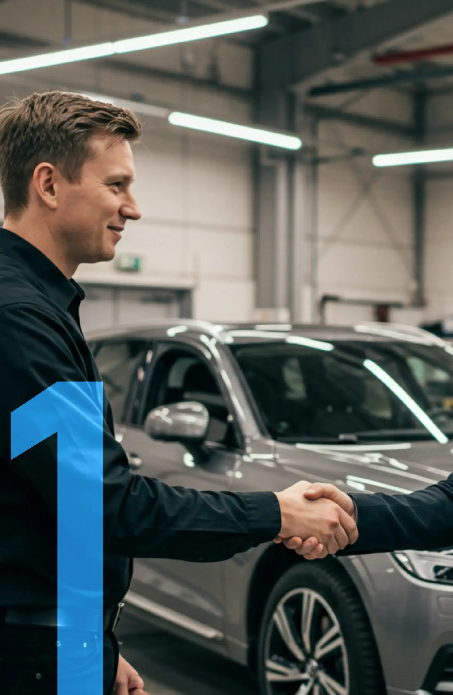 Dois homens apertam as mãos em frente a um carro em uma garagem.