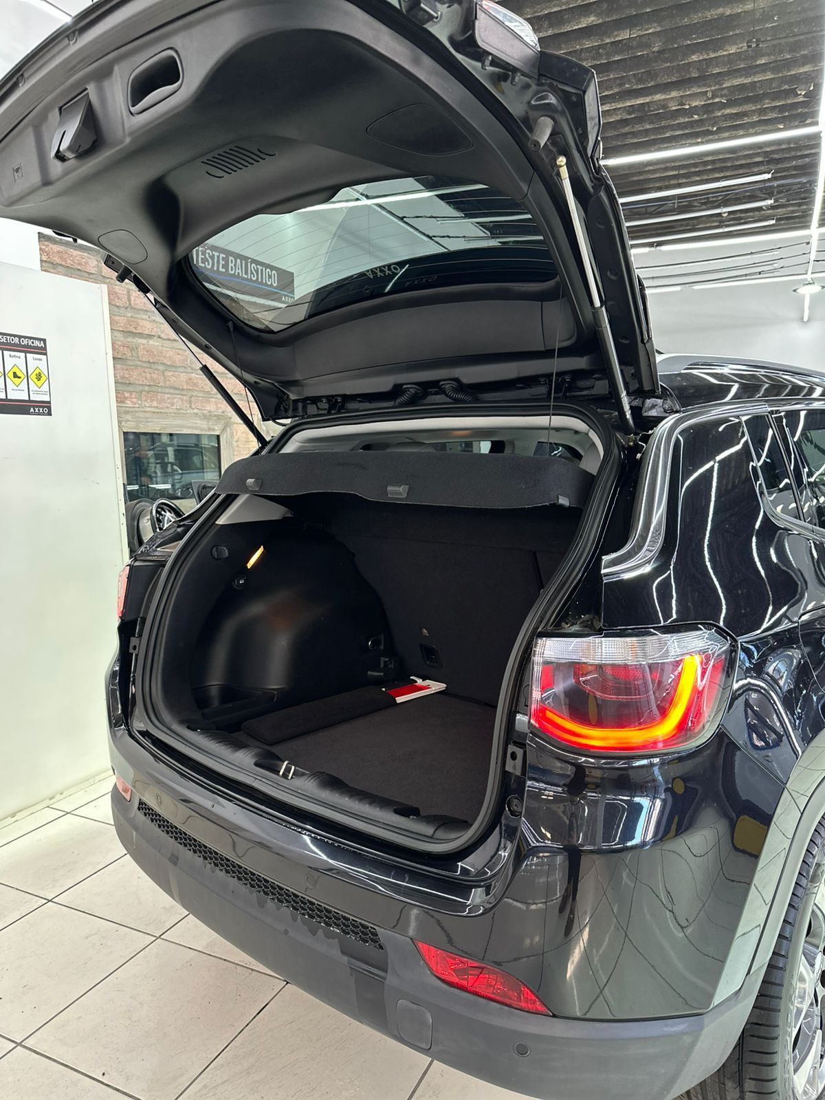 Abertura da traseira do Jeep Compass SUV preto, revelando o compartimento de carga. Lanterna traseira visível.