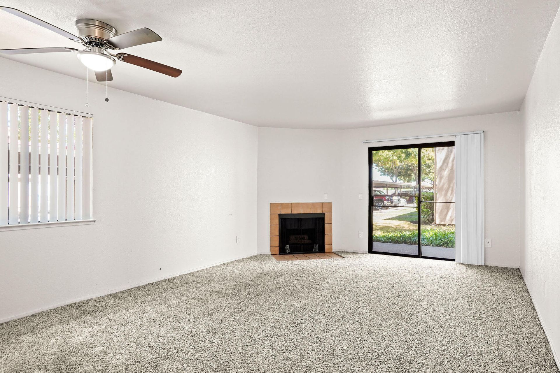 Empty carpeted living room with ceiling fan, fireplace, and sliding glass door to patio.