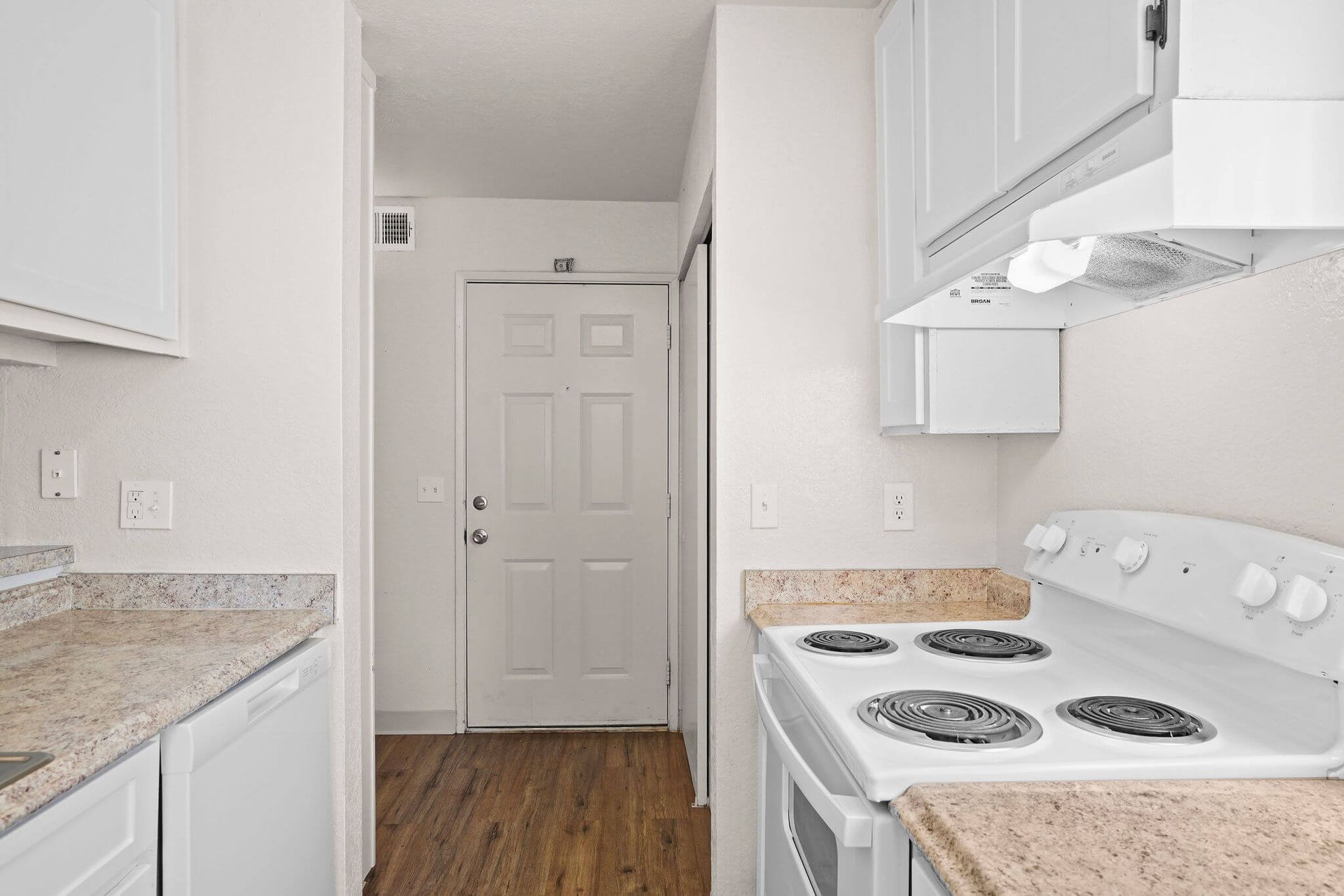 Bright white galley kitchen with granite counters, white appliances, and wood flooring leading to a back door