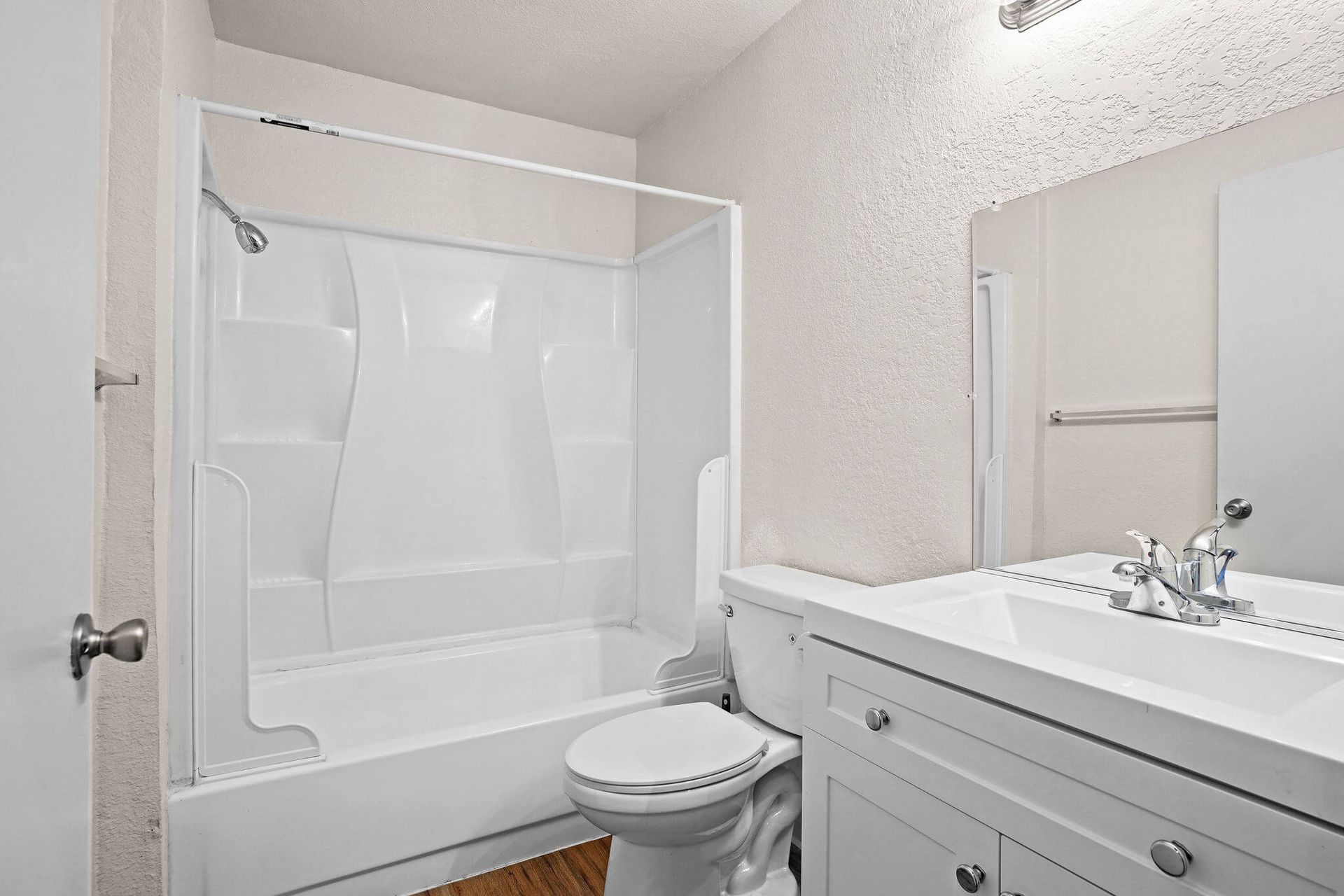 Bright bathroom with white tub-shower, toilet, and vanity with sink and mirror.