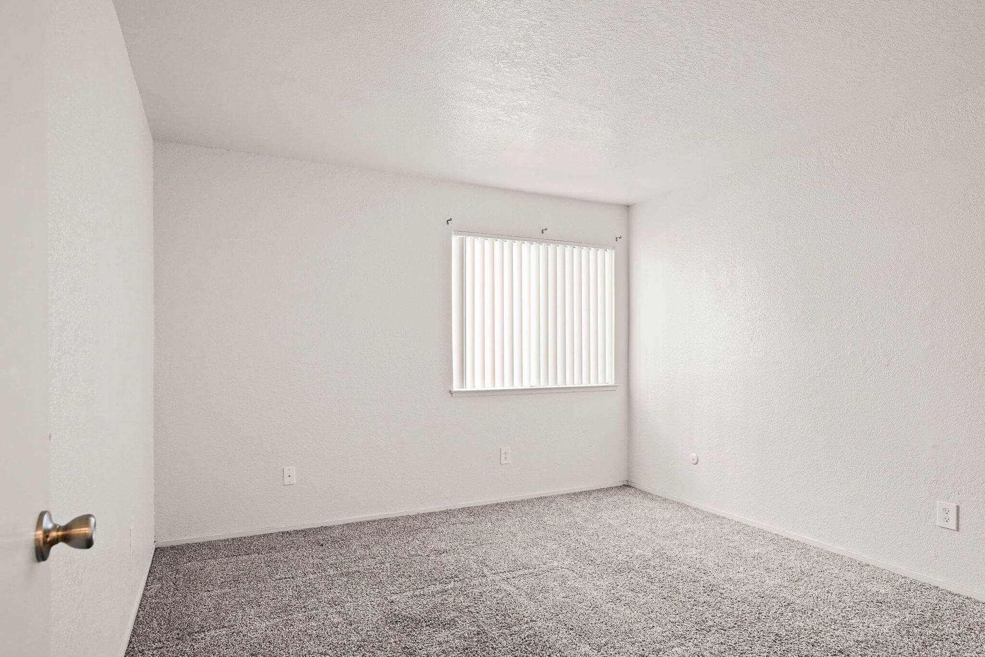 Empty white bedroom with carpeted floor and a window with vertical blinds